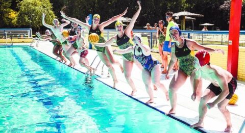 A group of waterpolo players mid-jump into a pool