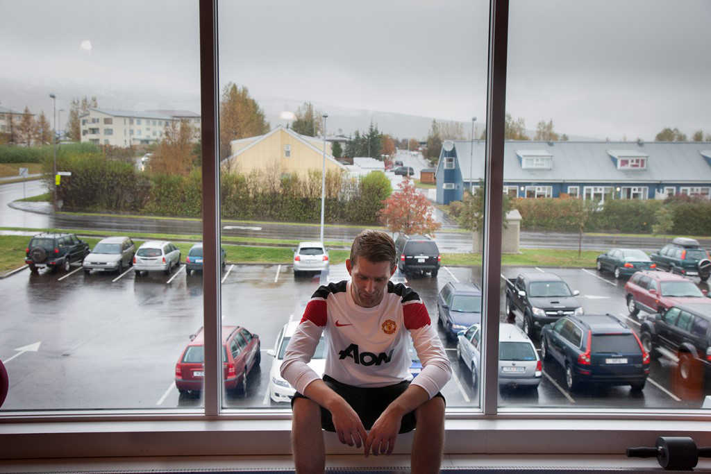 A man with MS in Iceland, sitting, with a car park behind him