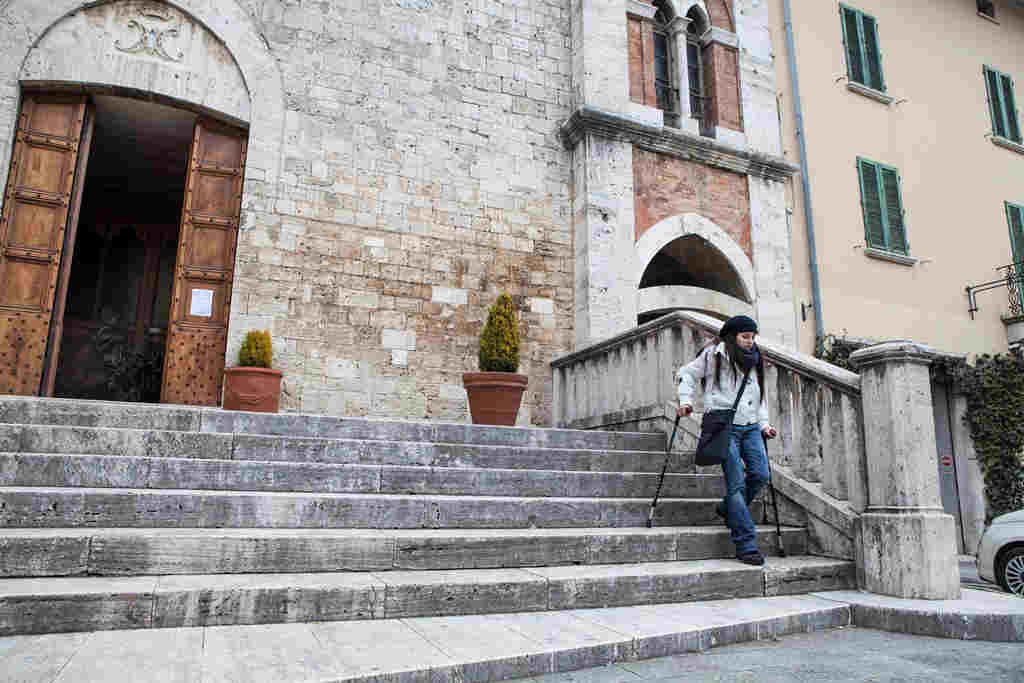 Woman using canes to descend steps to a public building in Italy