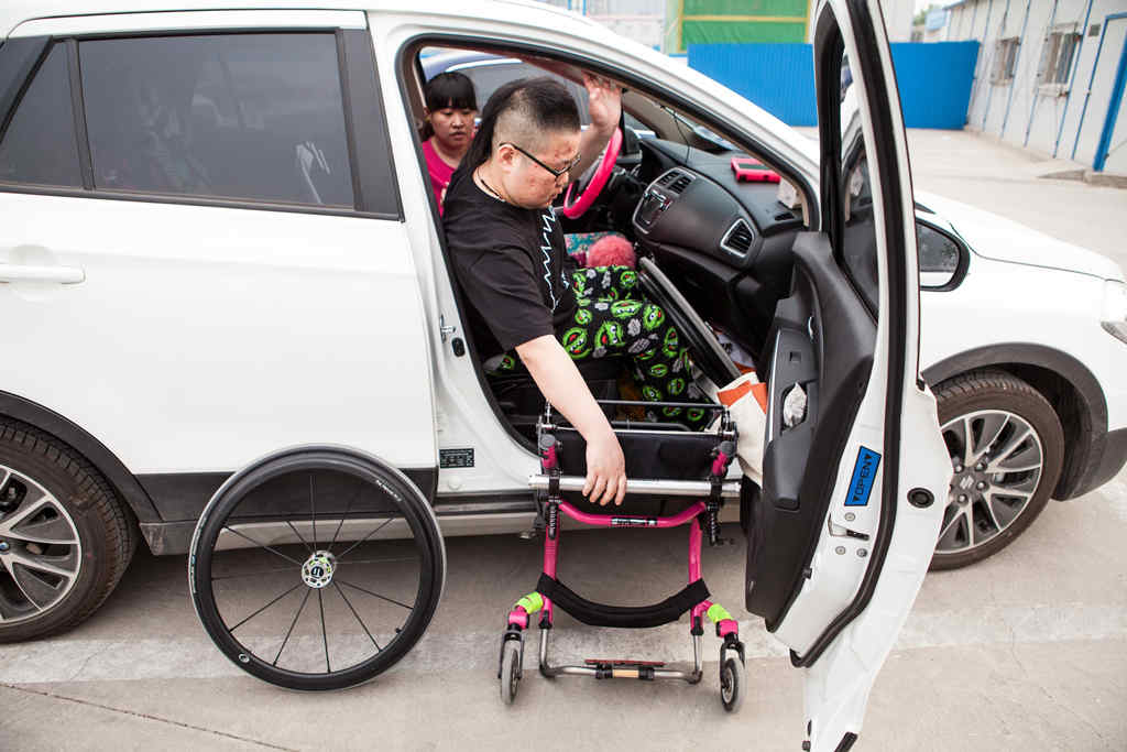 A young woman transfers herself from her wheelchair to her friend's car. She looks confident and comfortable
