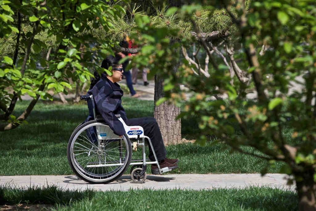 A woman in a wheelchair in a sunlit park in China