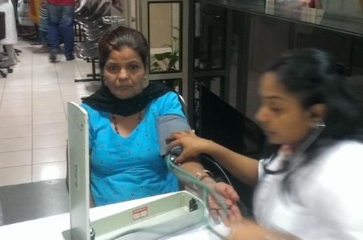 A woman in a blue dress watches as a woman checks her blood pressure