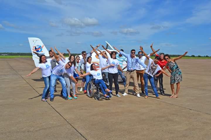 A group of people post with an airplane. Many of them have their arms outstretched mimicing the planes wings
