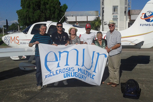 A small group of people stand in front of an airoplane holding a banner which reads 'EMUR'
