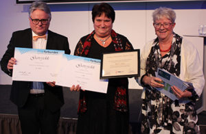 Bente stands smiling at the camera holding her award