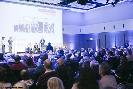 A large auditorium filled with an audience viewing a presentation projected on a screen at the front of the room.