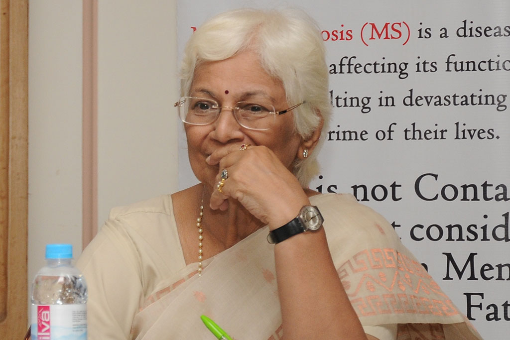 An Indian woman with white hair and glasses takes part in a panel discussion.